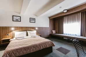 A hotel room with a large bed, wooden headboard, two bedside tables, a bench by the window, and a chair. - Hotel Rtanj Kopaonik (Raška)