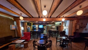 A cozy, rustic interior with wooden beams, a bar area, and seating arrangements.