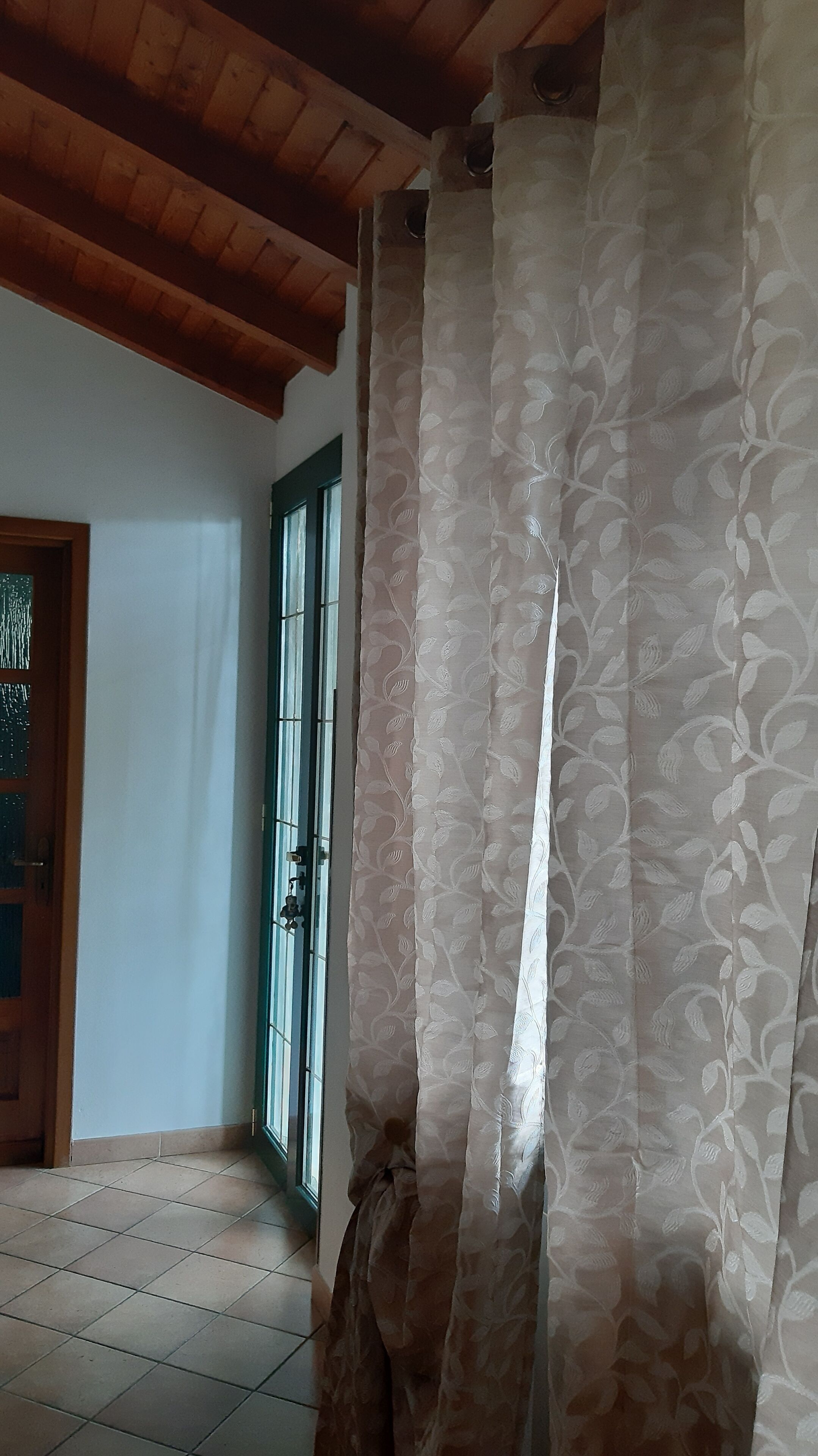 A room with a wooden ceiling, a patterned curtain, a tiled floor, and a door with a green frame.