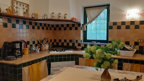 A kitchen with a checkered tile backsplash, a window with curtains, a stove, and various kitchen utensils. - Casa il Ciliegio (Terzorio)