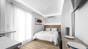 Een moderne hotelkamer met een houten vloer, een bed met witte lakens, een eettafel met borden en een glas, en een schilderij aan de muur.