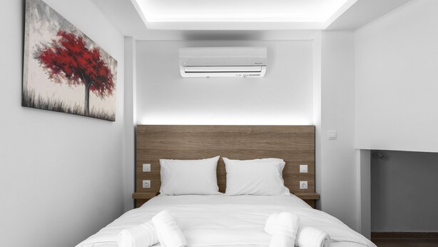 Een moderne hotelkamer met een opgemaakt bed, een wandairconditioner en een schilderij van een boom.