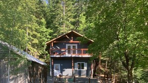 A two-story cabin with a balcony, surrounded by a forested area. - Gorgeous guest house, mature setting, 1 minute to the lake. (Harrison)