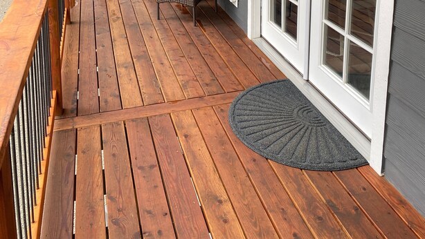 A wooden deck with a covered area, a sliding glass door, and outdoor furniture. - Gorgeous guest house, mature setting, 1 minute to the lake. (Harrison)