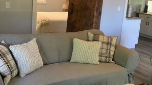 A living room with a gray sofa, several cushions, a coffee table with a rustic bowl, and a wooden barn door. - Gorgeous guest house, mature setting, 1 minute to the lake. (Harrison)