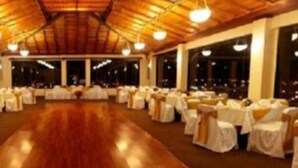 Une salle de banquet avec des tables et des chaises rondes, de grandes fenêtres et un plafond en bois.