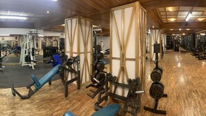 Une salle de sport équipée de divers appareils d’exercice, dotée d’un plancher en bois et de miroirs sur les murs.