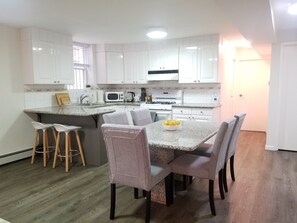 A modern kitchen with white cabinets, a granite countertop, and a dining area with four chairs. - Spacious 800 sqf 1BR, 2 minutes to subway + 6 minutes to Midtown Manhattan (Queens)