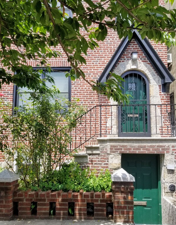A brick building with a green door, a small window, and a balcony with a metal railing. - Spacious 800 sqf 1BR, 2 minutes to subway + 6 minutes to Midtown Manhattan (Queens)