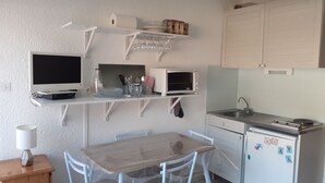 A compact kitchen with white cabinetry, a dining table, and a small refrigerator. - Studio Chaleureux en Montagne (Puyvalador)