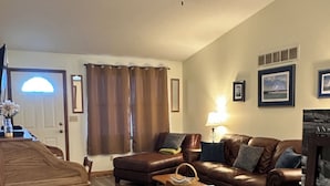 Un salon avec un canapé en cuir marron, une table basse en bois et un ventilateur de plafond.