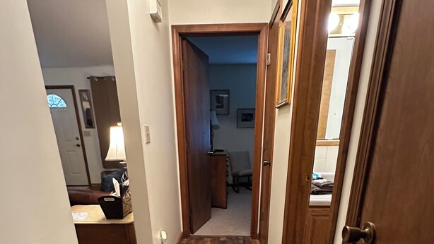 Un couloir doté d’un plancher en bois, un bureau avec une lampe et une porte donnant sur une autre pièce.
