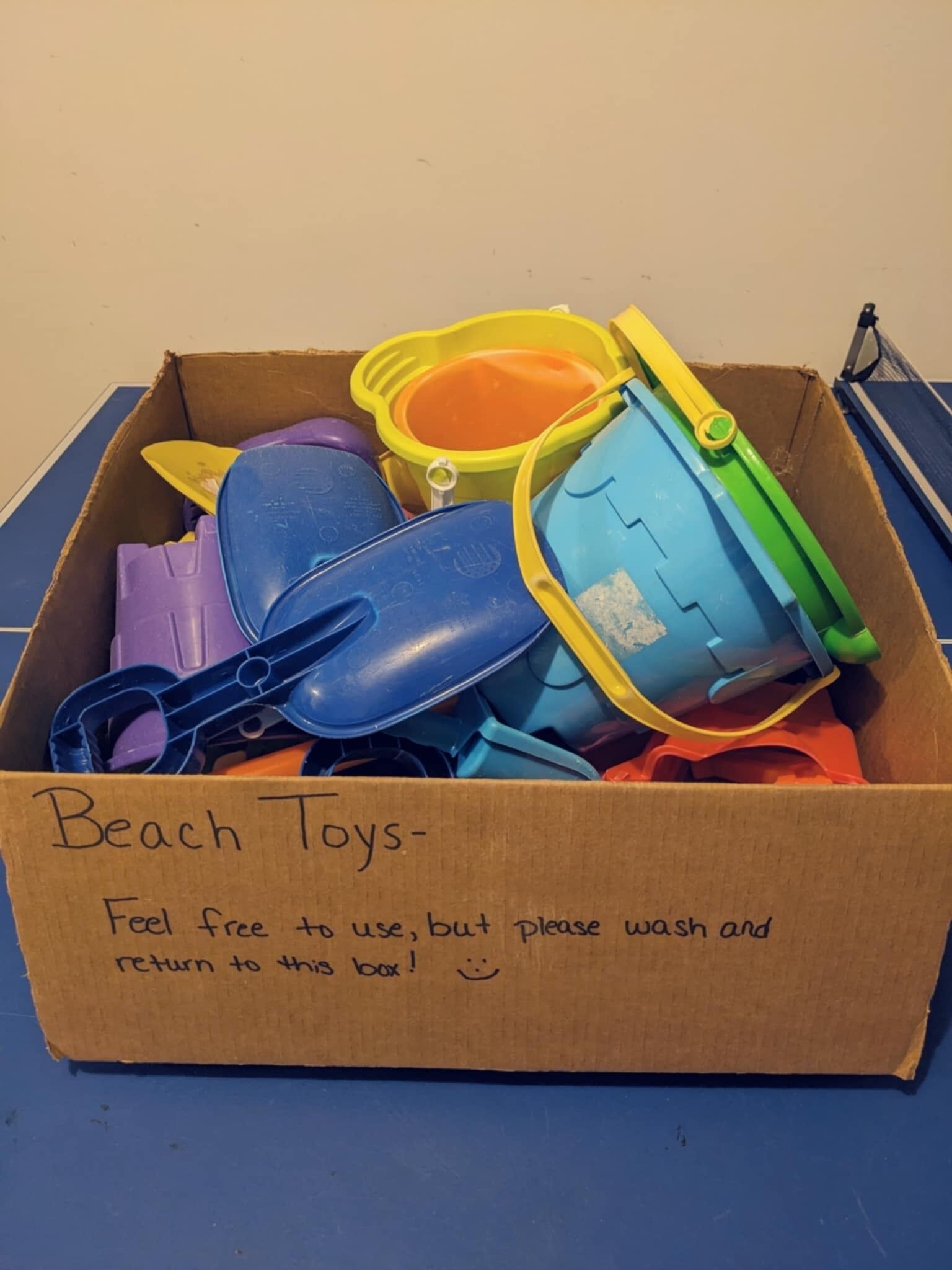 A cardboard box labeled "Beach Toys" with a note instructing to wash and return the toys.