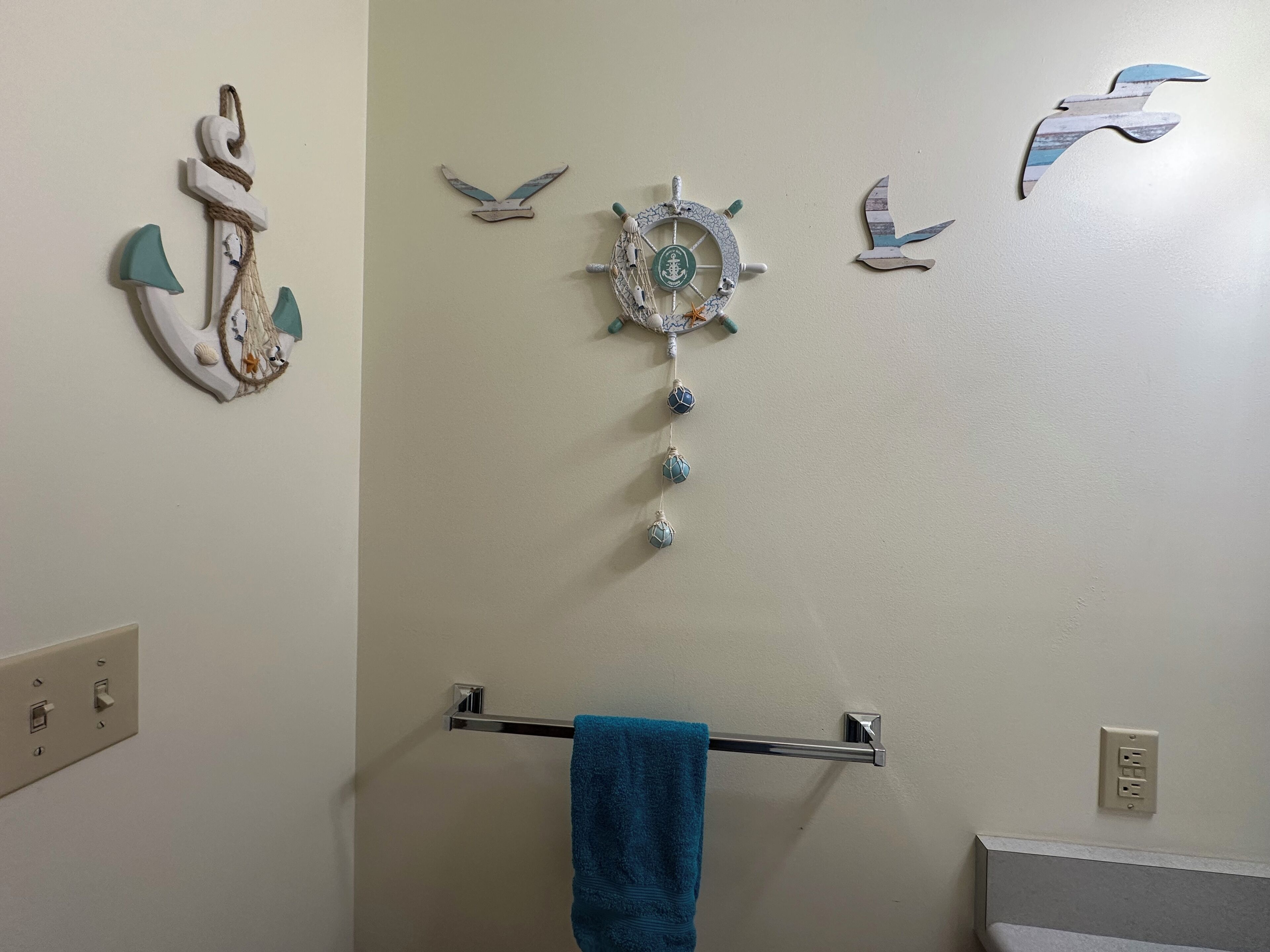 Une salle de bain avec un porte-serviettes, une décoration en forme de roue de navire et une décoration représentant un oiseau sur le mur.
