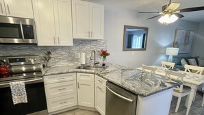 A modern kitchen with white cabinets, stainless steel appliances, a granite countertop, and a dining area with a white table and chairs.
