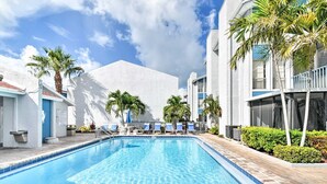 A swimming pool with lounge chairs and palm trees, surrounded by modern buildings.