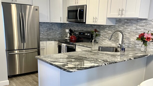 A modern kitchen with white cabinets, stainless steel appliances, a granite countertop, and a wooden floor.