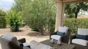 Une terrasse extérieure aménagée avec des meubles en osier, une table en bois et un jardin agrémenté d’arbres et d’arbustes.