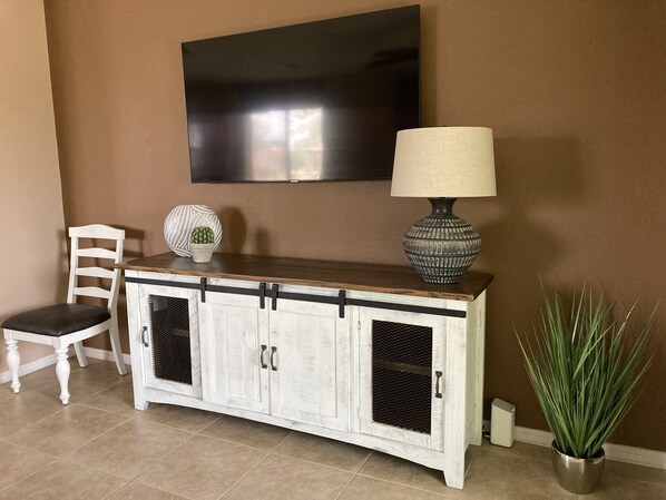 Un salon avec un meuble blanc, un téléviseur fixé au mur, une lampe, une chaise et une plante en pot.