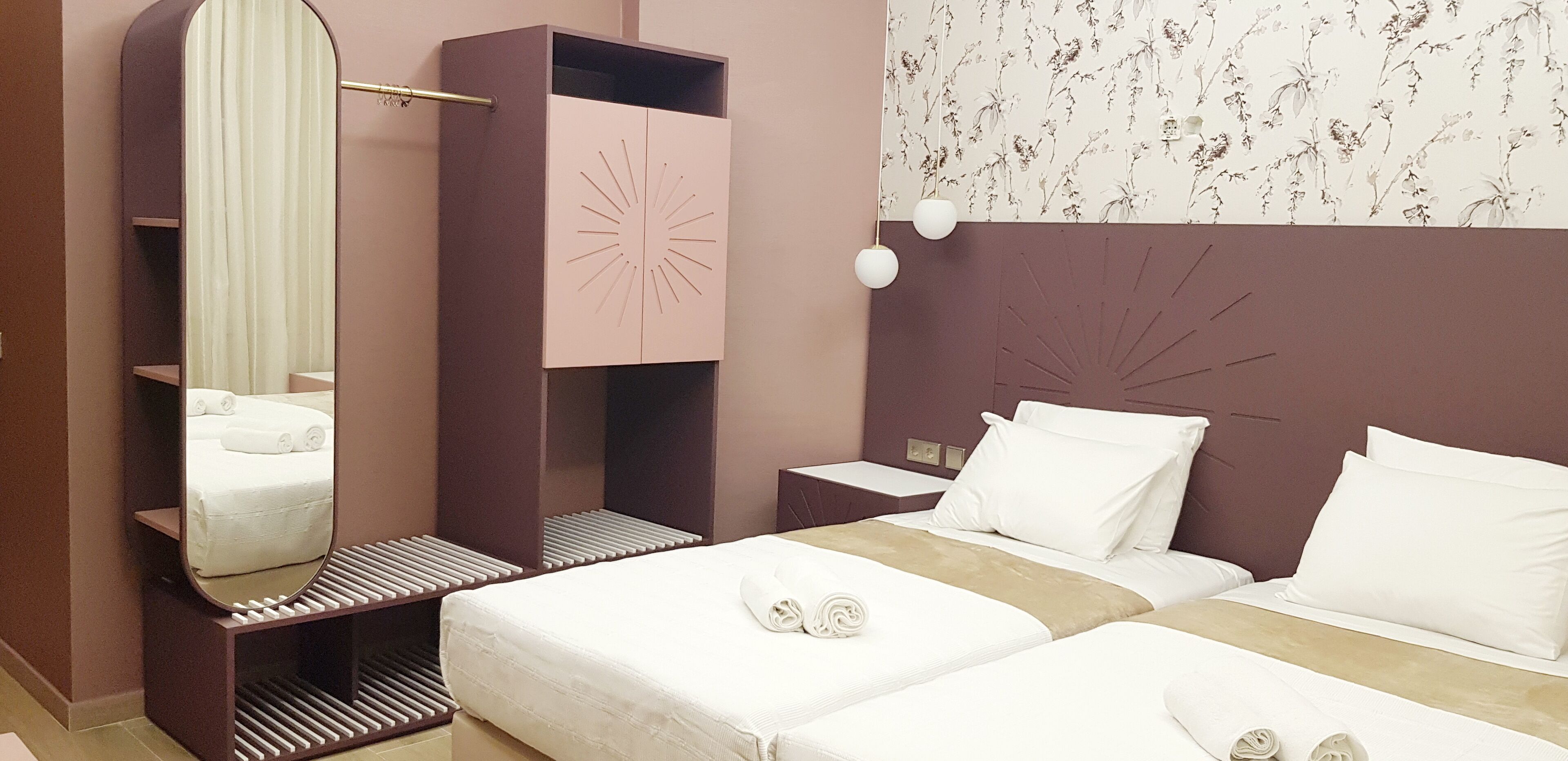A hotel room with a bed, a nightstand, a mirror, a wardrobe, and a wall with a floral pattern.