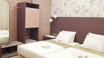 A hotel room with a bed, a nightstand, a mirror, a wardrobe, and a wall with a floral pattern.