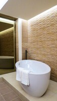 A modern bathroom with a freestanding bathtub, a towel draped over it, and a tiled wall.