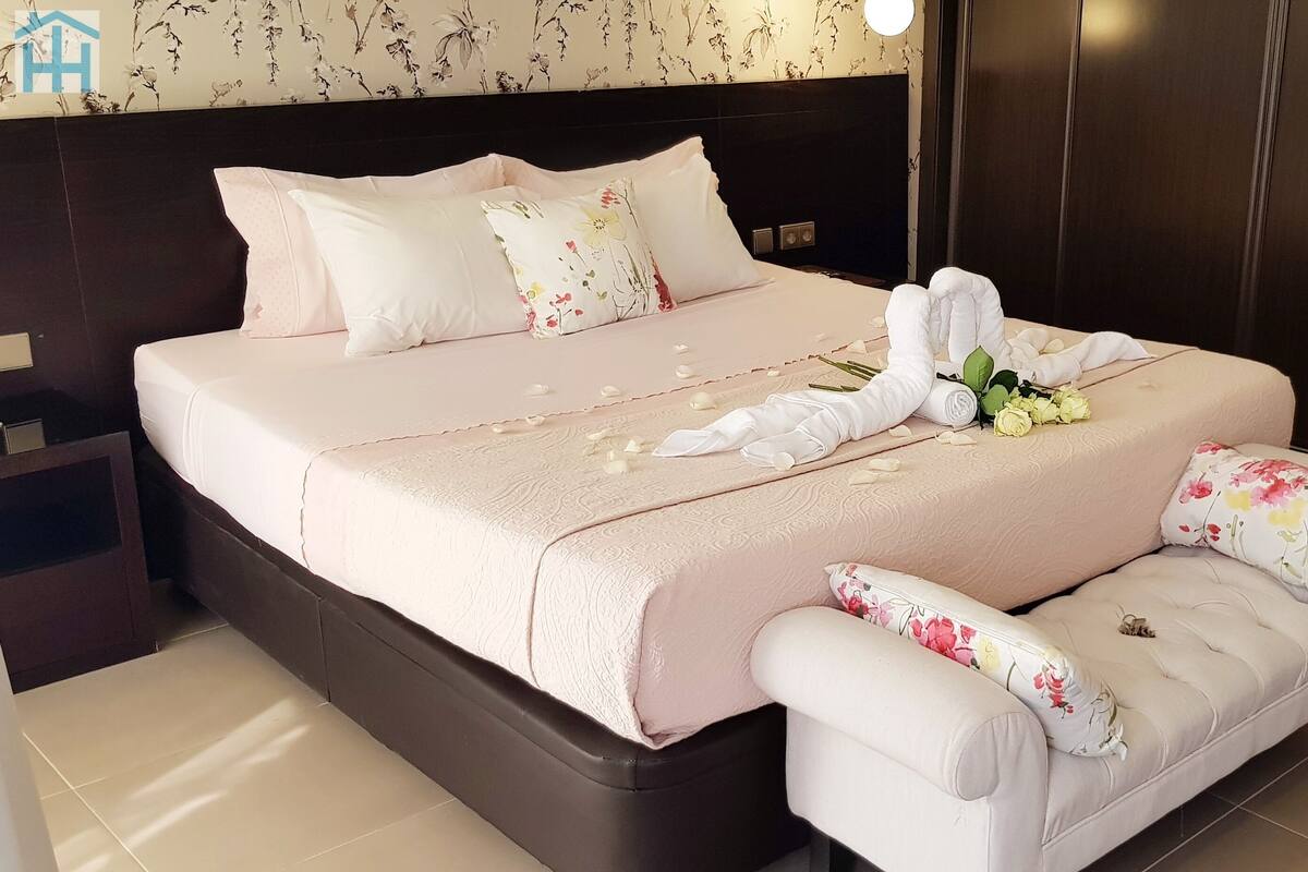 A neatly made bed with floral pillows, a bedside table, and a small sofa with floral cushions.