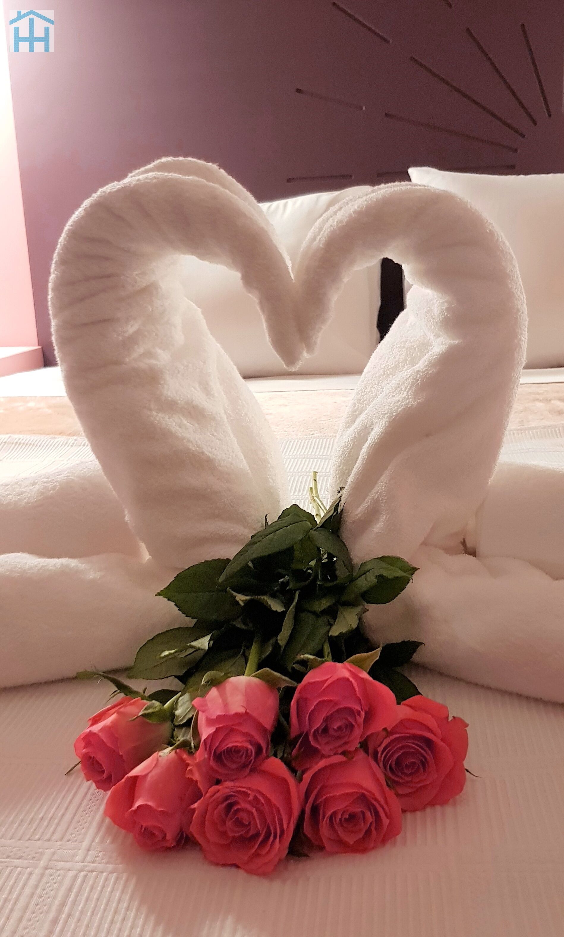Un lit avec du linge de lit blanc et une serviette pliée en forme de cœur.