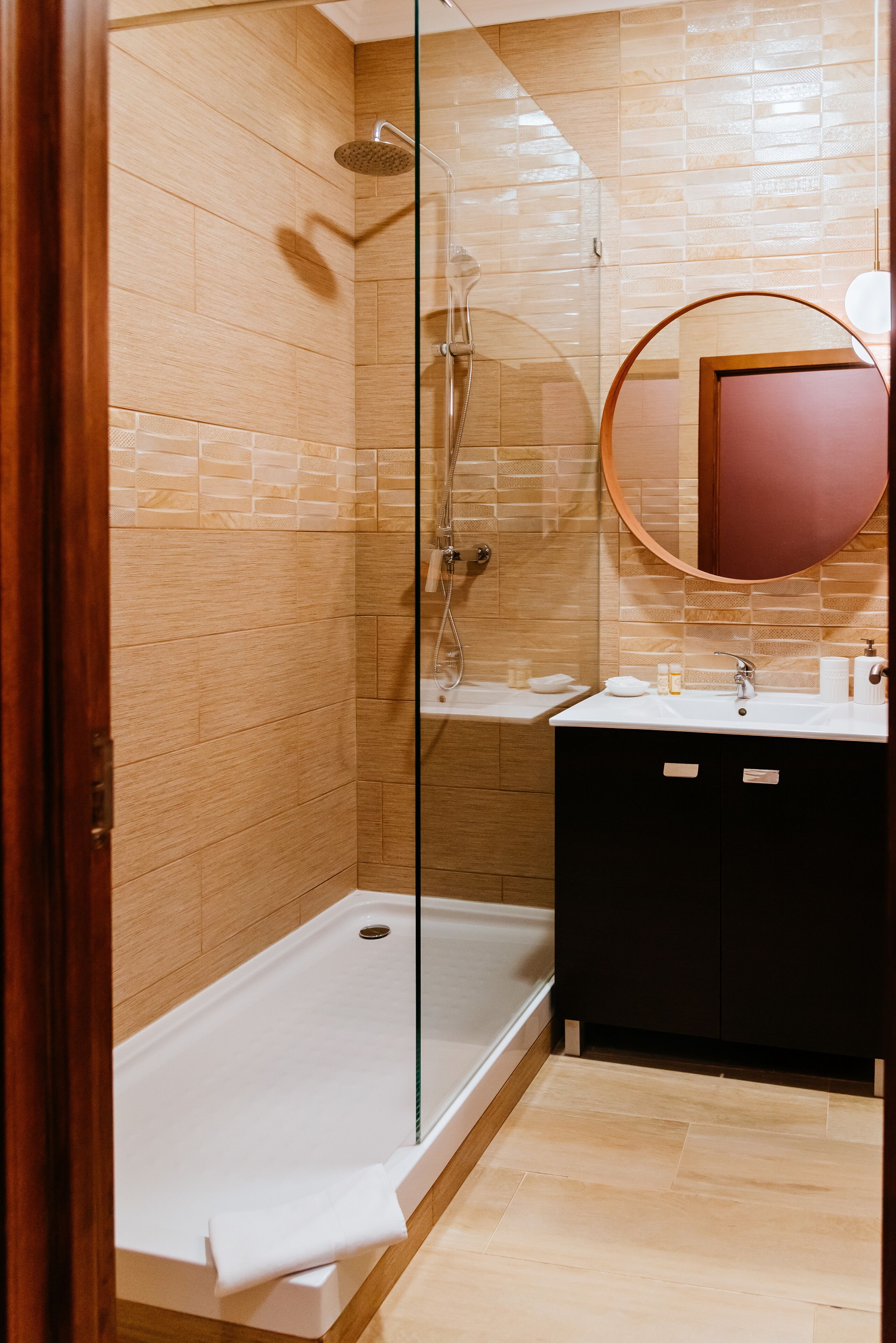 A modern bathroom with a glass-enclosed shower, a white sink, and a round mirror.