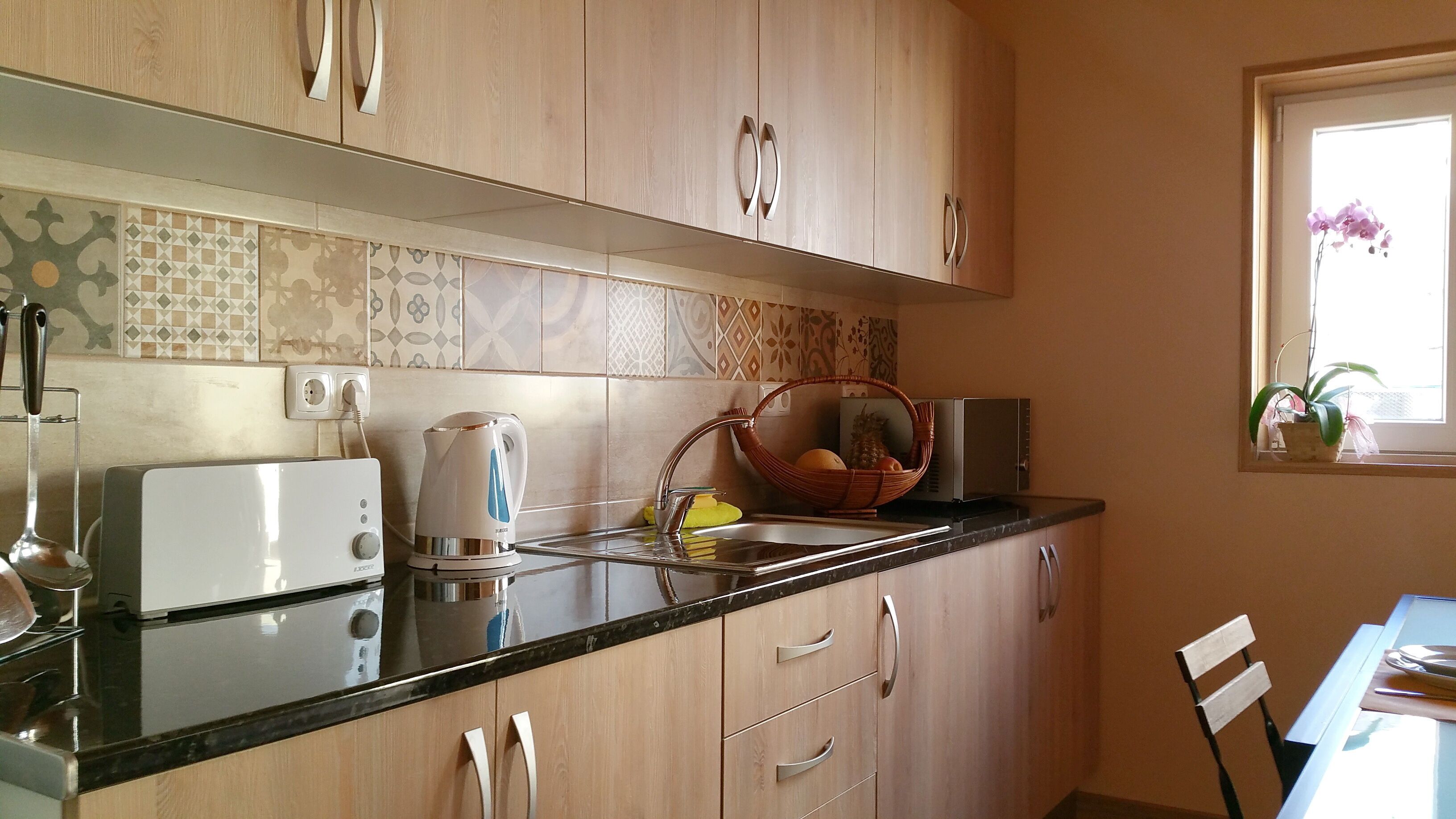 A kitchen with wooden cabinets, a black countertop, a kettle, a toaster, and a window with a plant.