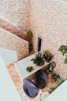 An outdoor patio with a brick wall, potted plants, and wicker furniture.