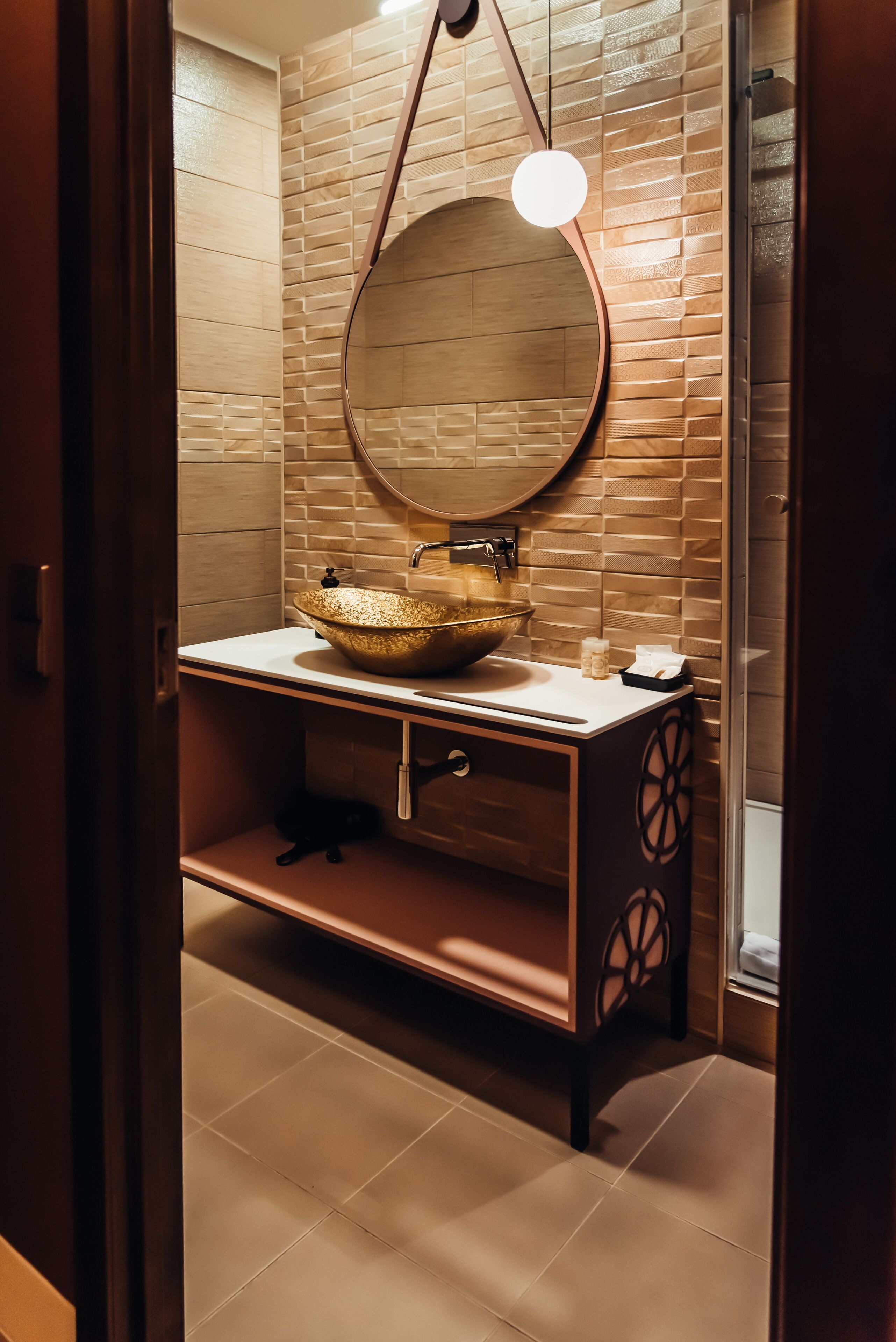 A bathroom with a round mirror, a gold bowl sink, and a wooden vanity.