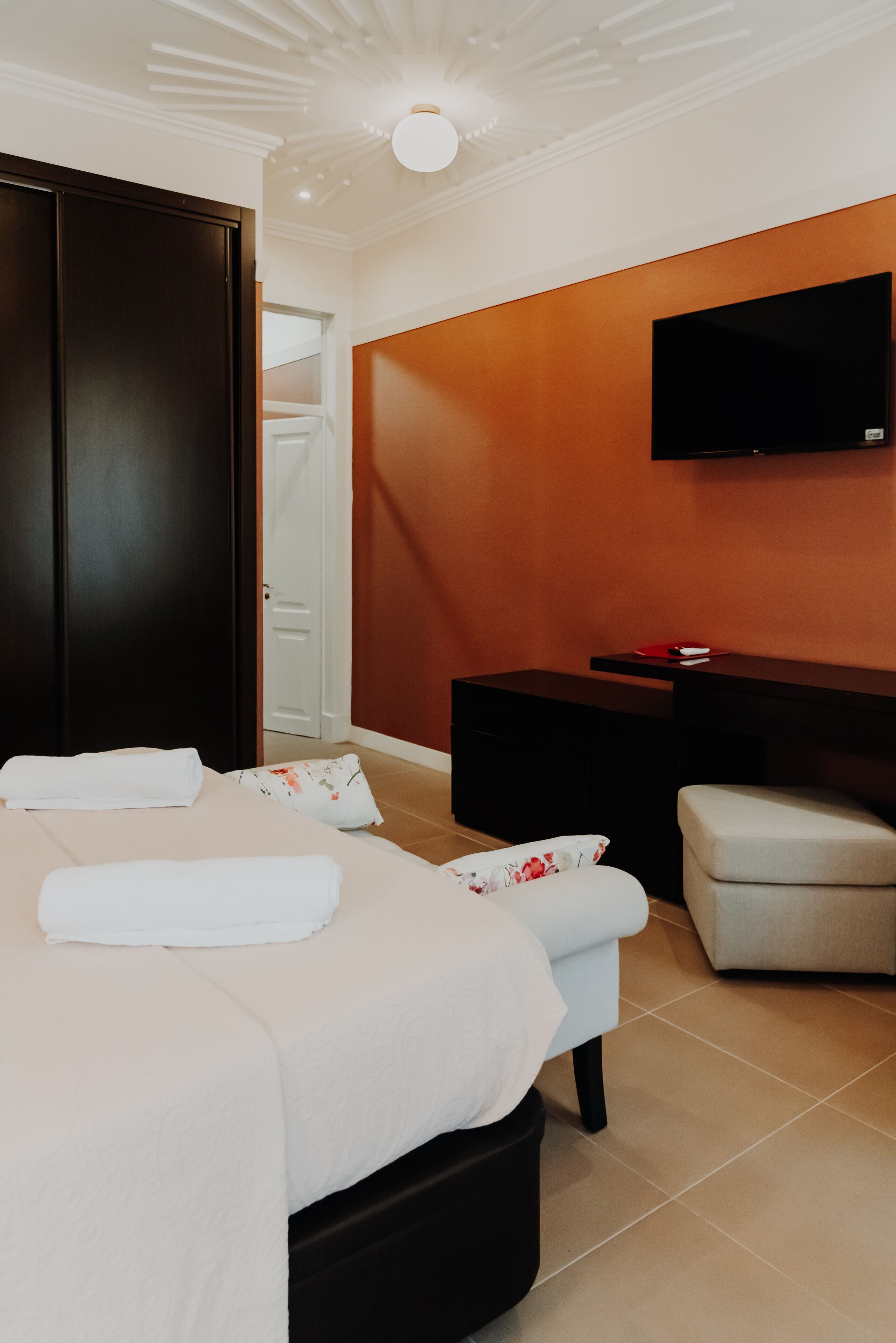 A modern hotel room with a bed, a desk, a TV, and a wardrobe.