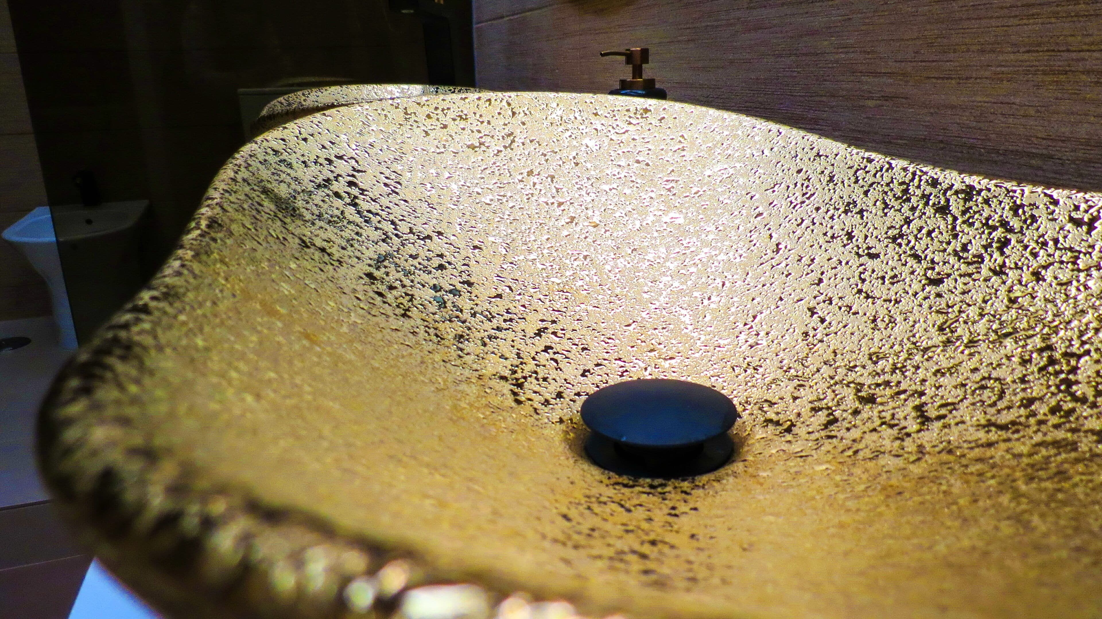 A close-up of a textured, golden-colored sink with a black drain.