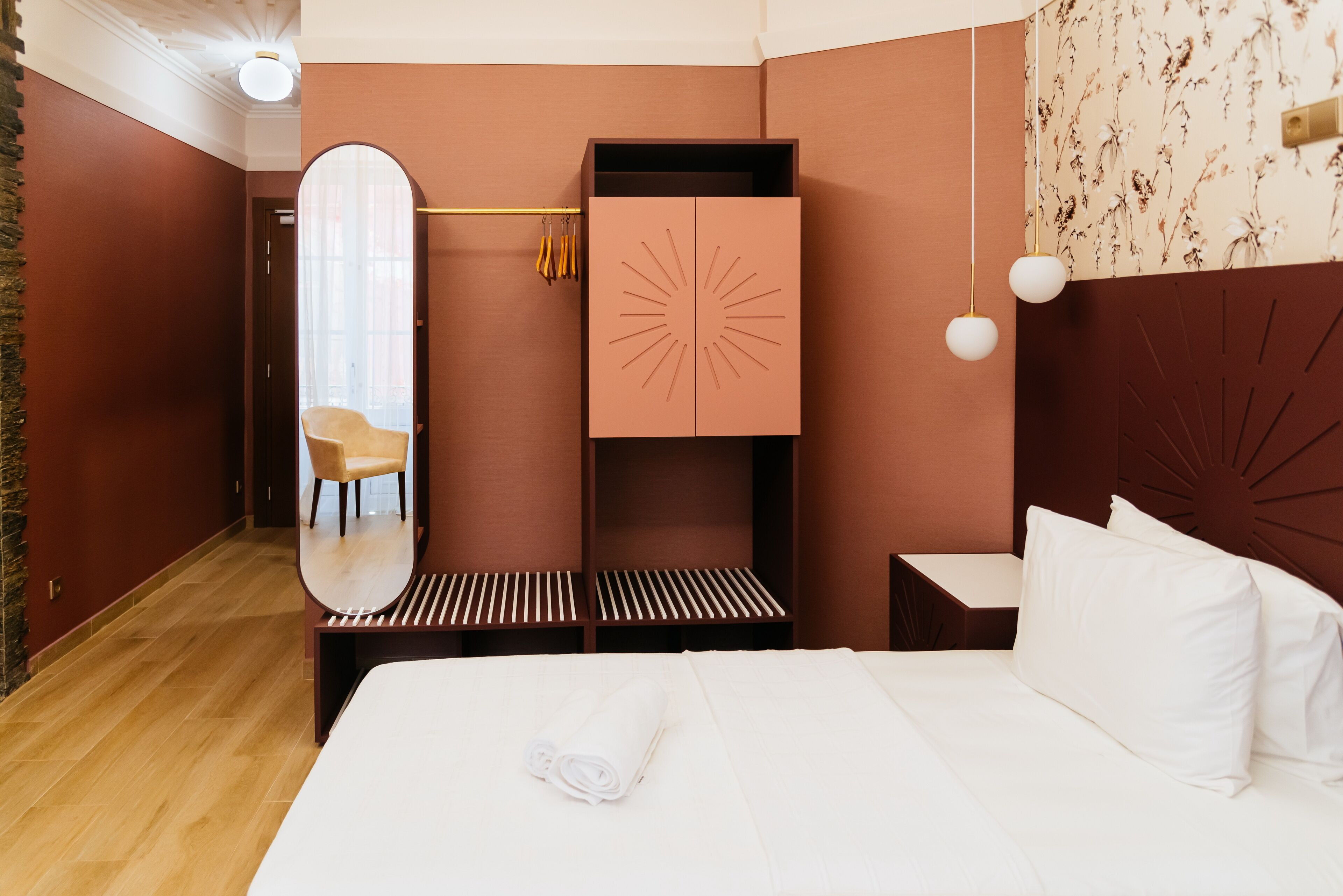 Une chambre d’hôtel avec un lit, un banc en bois, un miroir et une armoire.