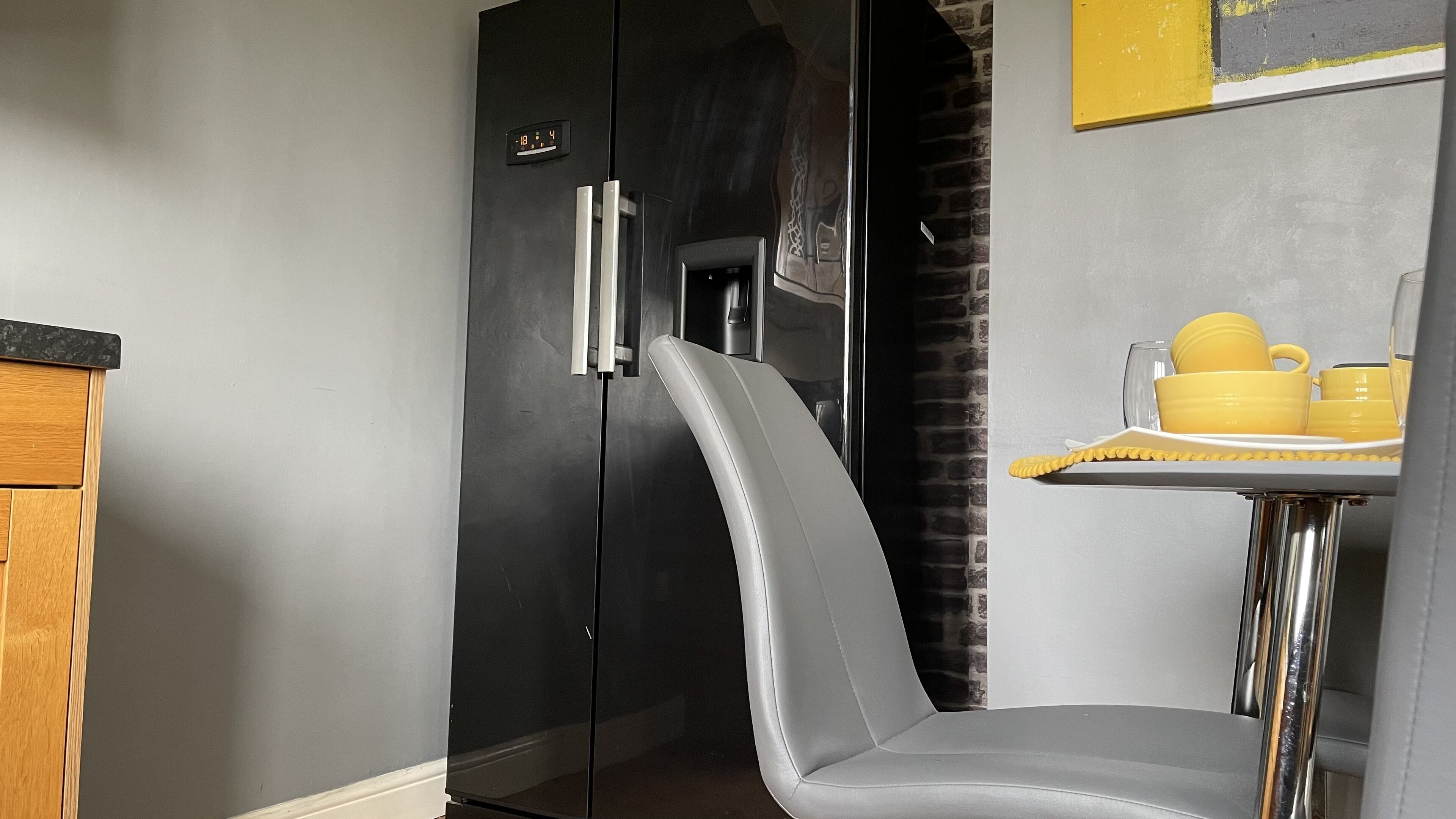 Une cuisine moderne avec un réfrigérateur noir, une chaise grise et un plateau jaune contenant des tasses et un verre.