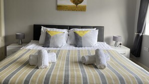 Siististi pedattu sänky, jossa on raidallinen vuodevaatesetti, kaksi yöpöytävalaisinta ja sydämenmuotoinen taulu seinällä.