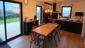 Eine moderne Küche mit Holztisch und -stühlen, einer Kaffeemaschine und Blick ins Freie durch große Fenster.