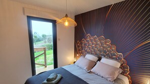 Ein Schlafzimmer mit einem großen Bett, Blick ins Freie durch eine Glastür und einem außergewöhnlichen Wanddesign.