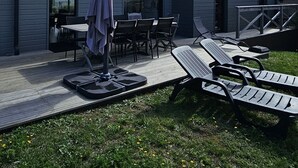 Ein modernes Gebäude mit einer Terrassenfläche, die Gartenmöbel und eine überdachte Sitzgelegenheit bietet.