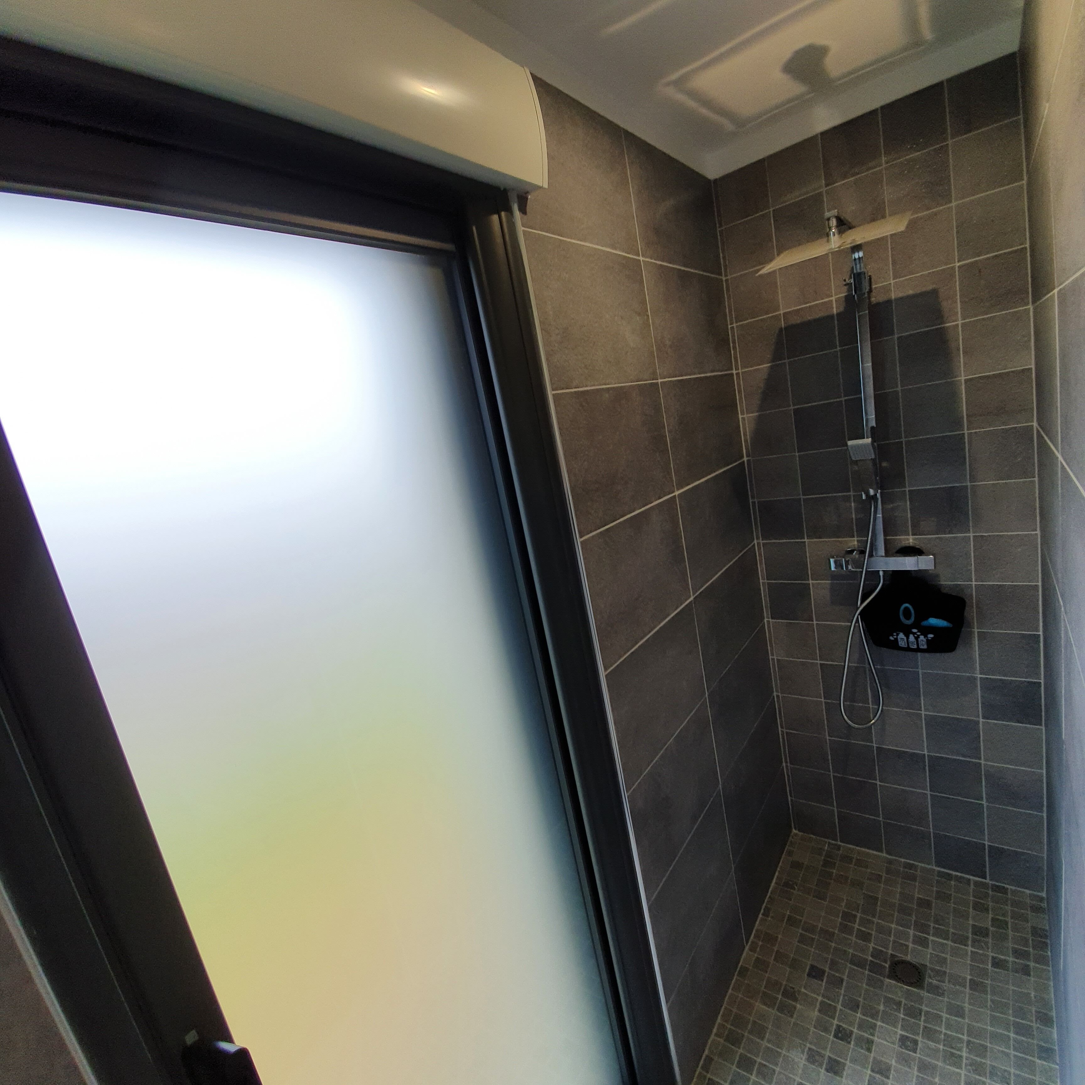 Un baño moderno con ducha, paredes de azulejos y puerta de vidrio esmerilado.