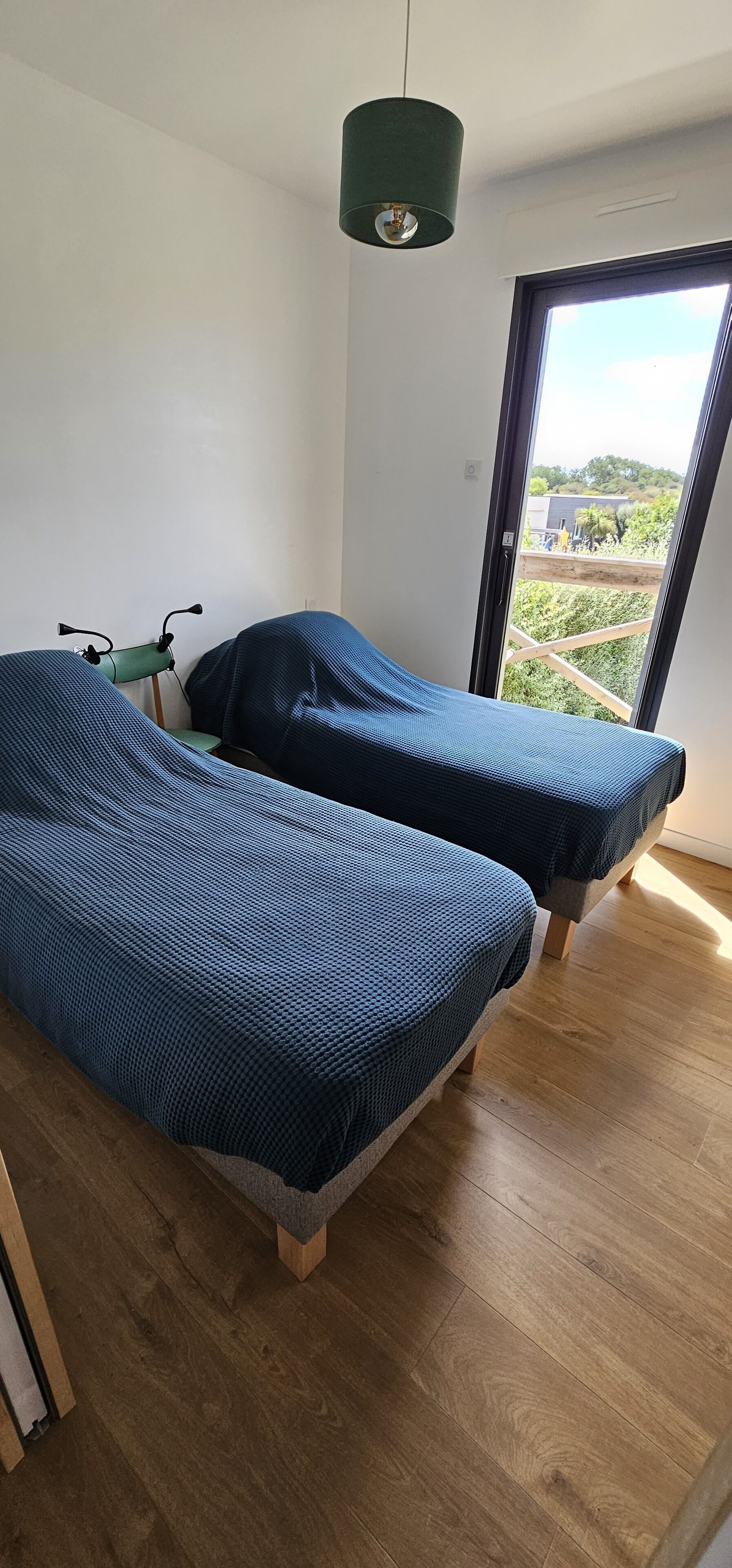 Una habitación con dos camas, una lámpara verde y vistas al verdor exterior.