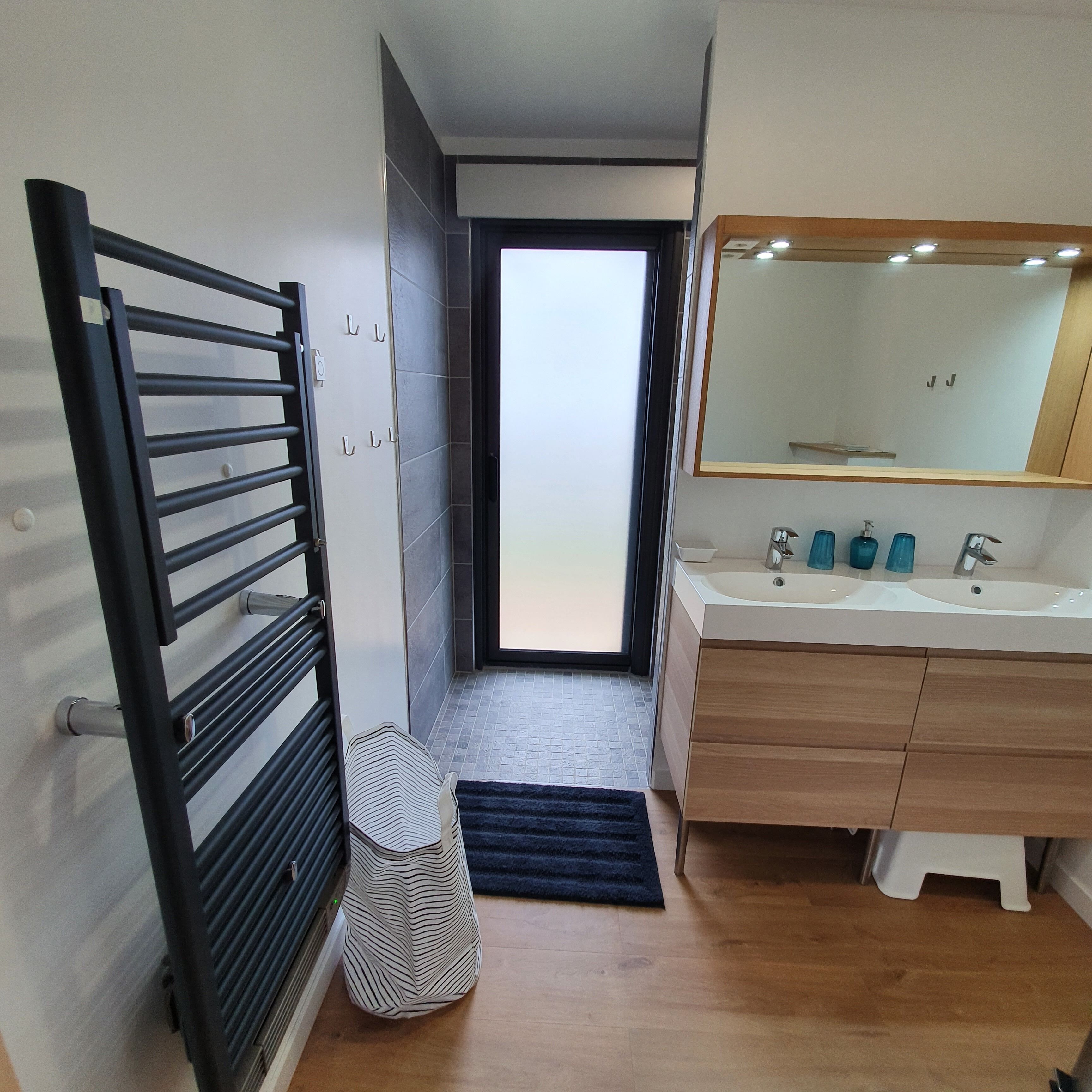 Un baño moderno con tocador de madera, un espejo grande y un lavamanos.