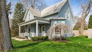A two-story house with a front porch, a covered entryway, and a well-maintained lawn. - (2027 OPEN!) New Buffalo Home With Private Pool and Hot Tub! (New Buffalo)