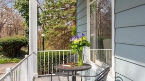 A covered outdoor area with a round table, a chair, and a vase with flowers. - (2027 OPEN!) New Buffalo Home With Private Pool and Hot Tub! (New Buffalo)
