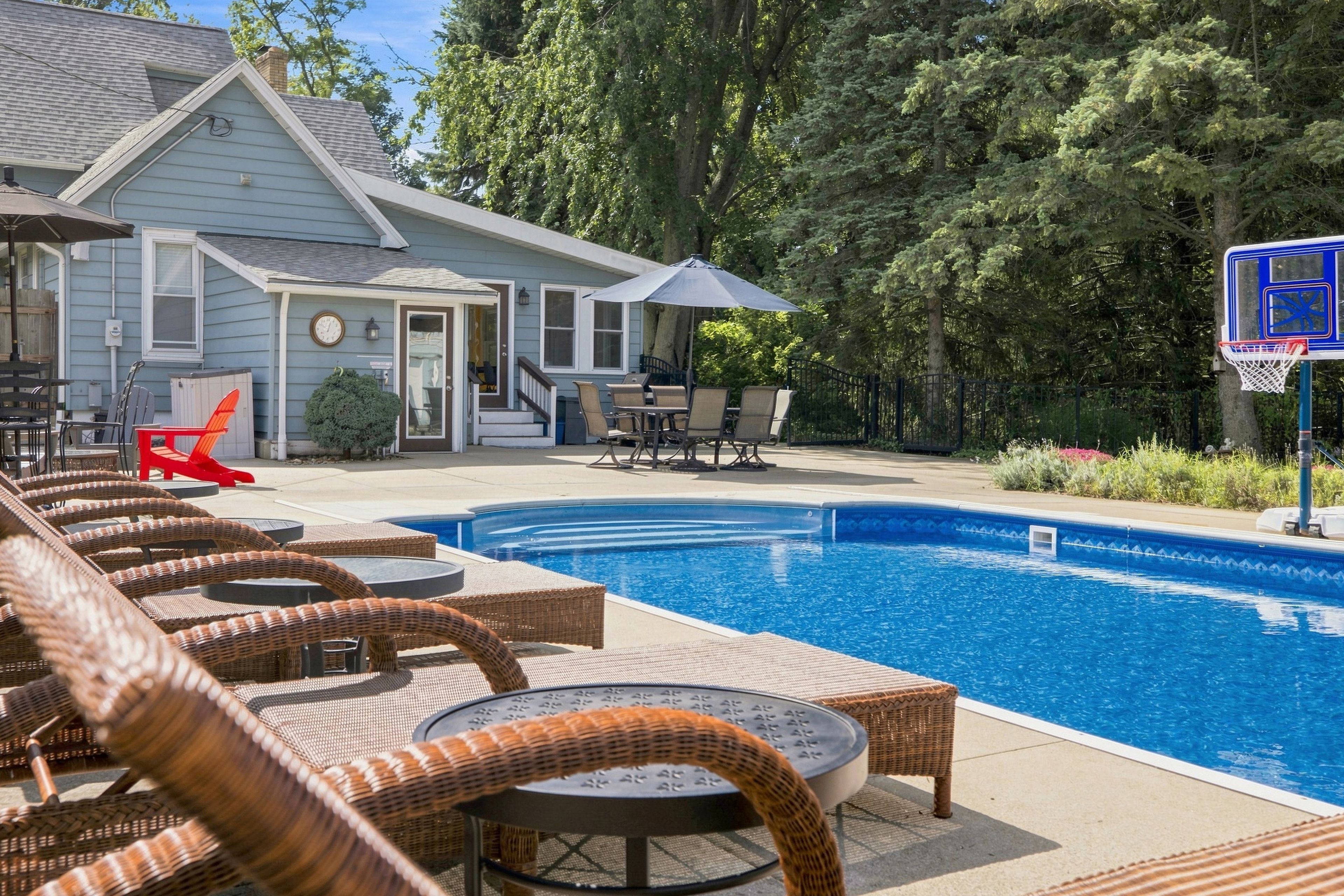 A swimming pool area with lounge chairs, a basketball hoop, and a building in the background.