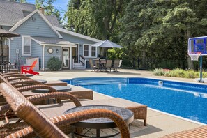 Un espace piscine avec des chaises longues, un panier de basketball et un bâtiment en arrière-plan.
