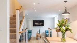 A modern living room with a staircase, a flat-screen TV, and a decorative vase. - The Escape (Brighton)