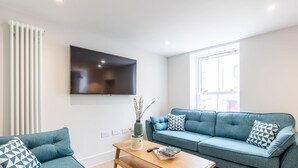 A modern living room with a sofa, a coffee table, a TV, and a window. - The Escape (Brighton)