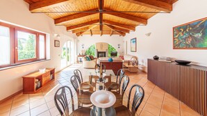 A spacious living room with a high wooden ceiling, a dining area with a glass table, and a kitchen in the background. - Beautiful Villa with Private Pool and Garden (Massa Lubrense)